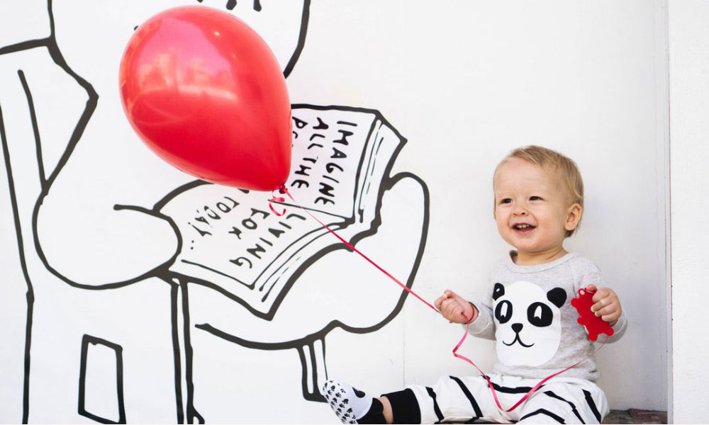 child holding onto red balloon smiling