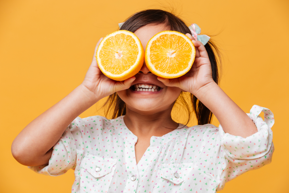 kid holding orange before eating for vitamins for teeth