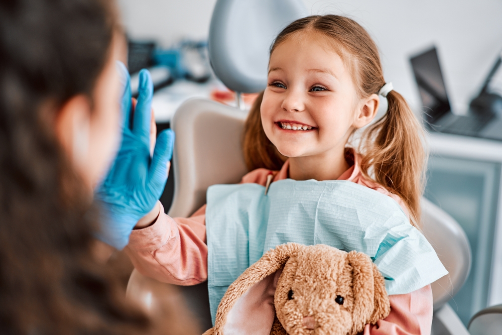 Smiling young girl giving a high five to a dentist while holding a stuffed toy